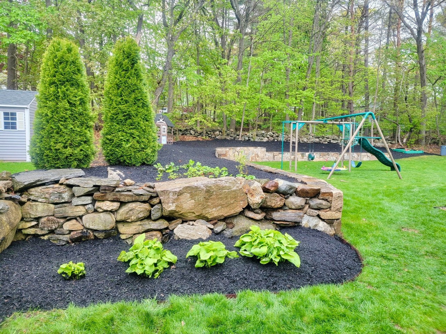 Fresh black mulch installed around stone landscape walls and garden beds in Massachusetts